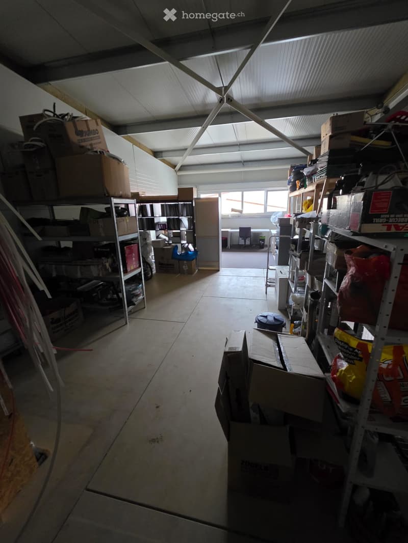 Storage room: large, empty room with metal shelving units, various storage boxes, a trash bin, windows, and a doorway