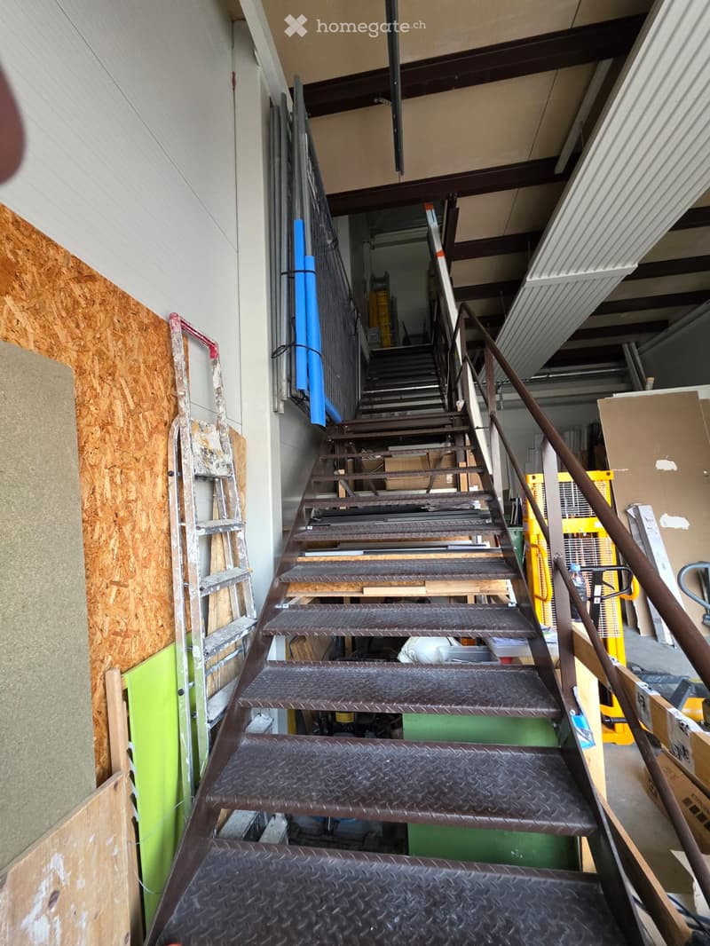 Industrial building under construction, metal stairs with rubber mats, white and brown walls, wooden and metal structures, storage boxes, ladders, boxes, blue poles