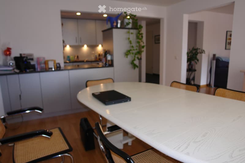 Dining area with round table, chairs, central kitchen island, potted plants, and framed artwork