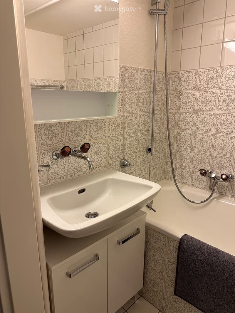 Bathroom with white tiles, white sink, bathtub, and towel
