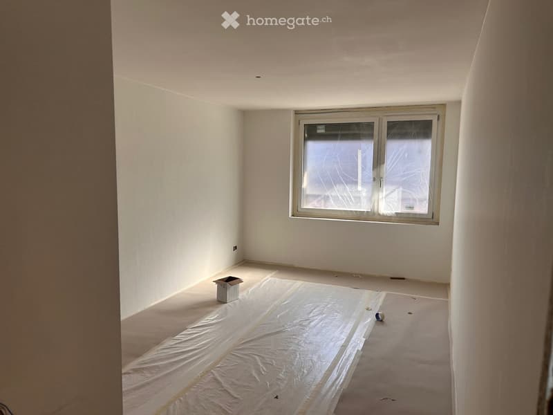 An empty room with white walls, a large window, and a white sheet covering the floor.