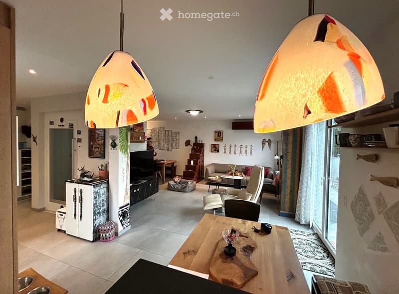 Living room with a large open space, modern furnishings, and a wooden table. Two unique pendant lights.