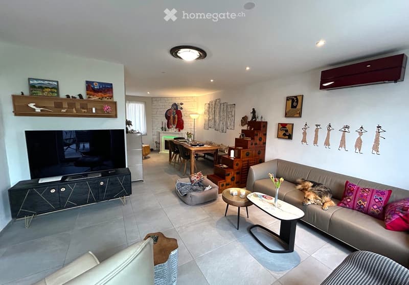 A living room with a grey couch, coffee table, floor lamps, TV, dining table, and a kitchen area