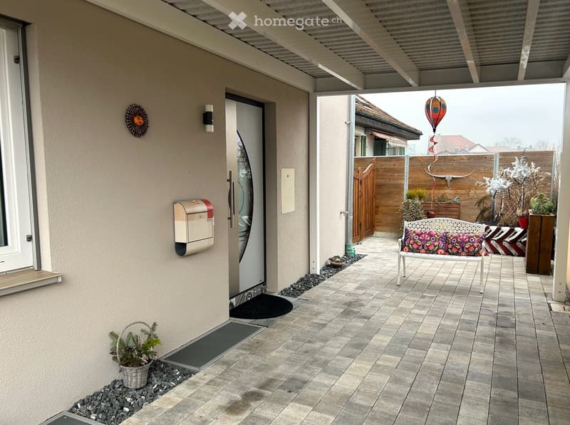 Covered patio with brick floor, wooden fence, wooden bench, decorative plants, mailbox
