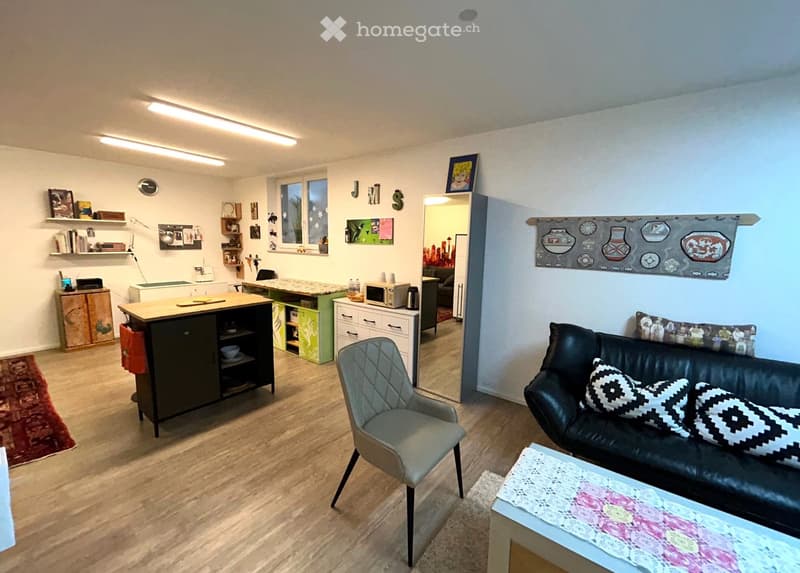Living room with wooden floor, black leather sofa, coffee table, side table, armchair, wooden table with drawers, kitchen table, shelves, radiator, open door, mirror, painting, wall hanging