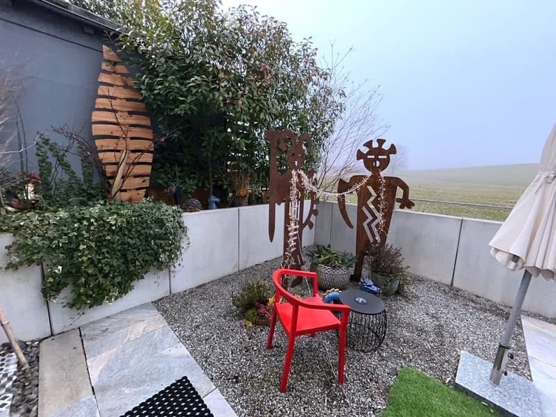 gravel ground, red chair, round table, concrete wall, plants, decorative sculptures, open view