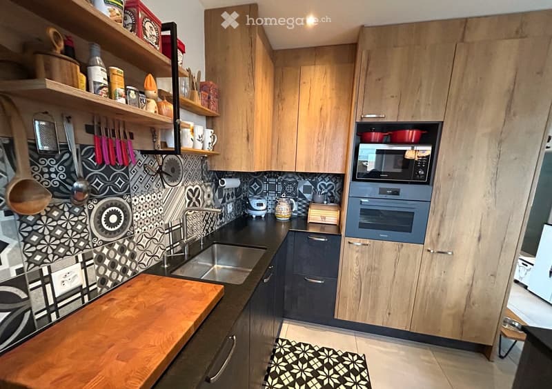 modern kitchen with black countertop, wooden cabinets, white tile backsplash, wooden cutting board, stainless steel sink and faucet, microwave, oven