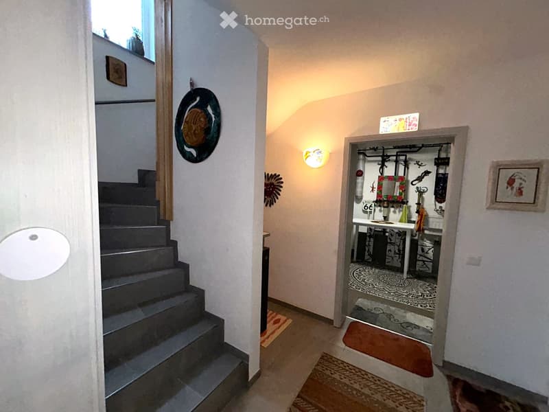 A house hallway with stairs leading to a lower level, a room with a desk and rug, and a framed picture on the wall.