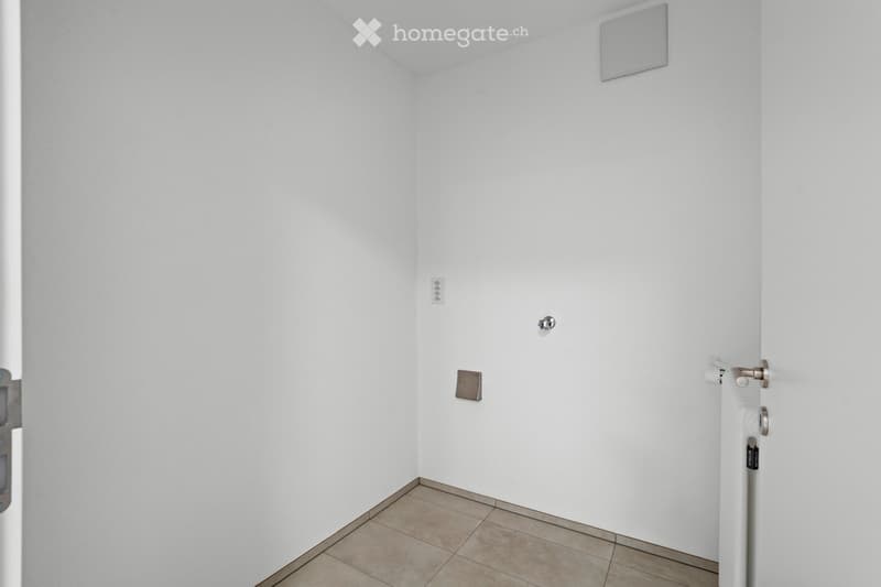 empty room with white walls, tiled floor, electrical socket, and silver objects on the wall