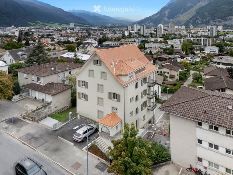 Apartmens in city, car parking space in front, brown rooftop, mountains background