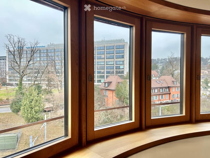 Bay window with wooden frame and three windows overlooking a building, trees, and landscape outside