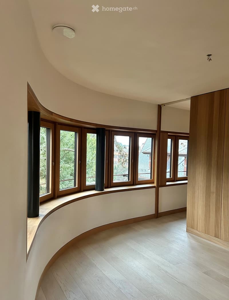 Room with wooden curved benches along large windows, wooden floor, light fixtures.