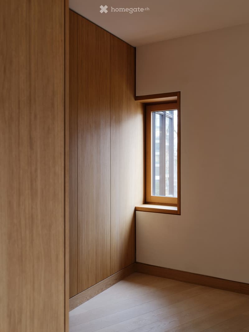 Empty room with wooden walls, light wooden floor, and a small window letting in natural light.