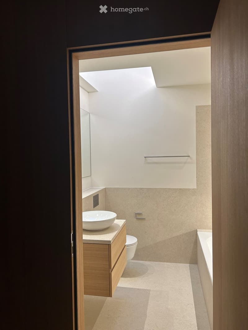 Bathroom with wooden vanity, white sink, white toilet, bathtub, tiled flooring, mirror, skylight, stainless steel towel rack.