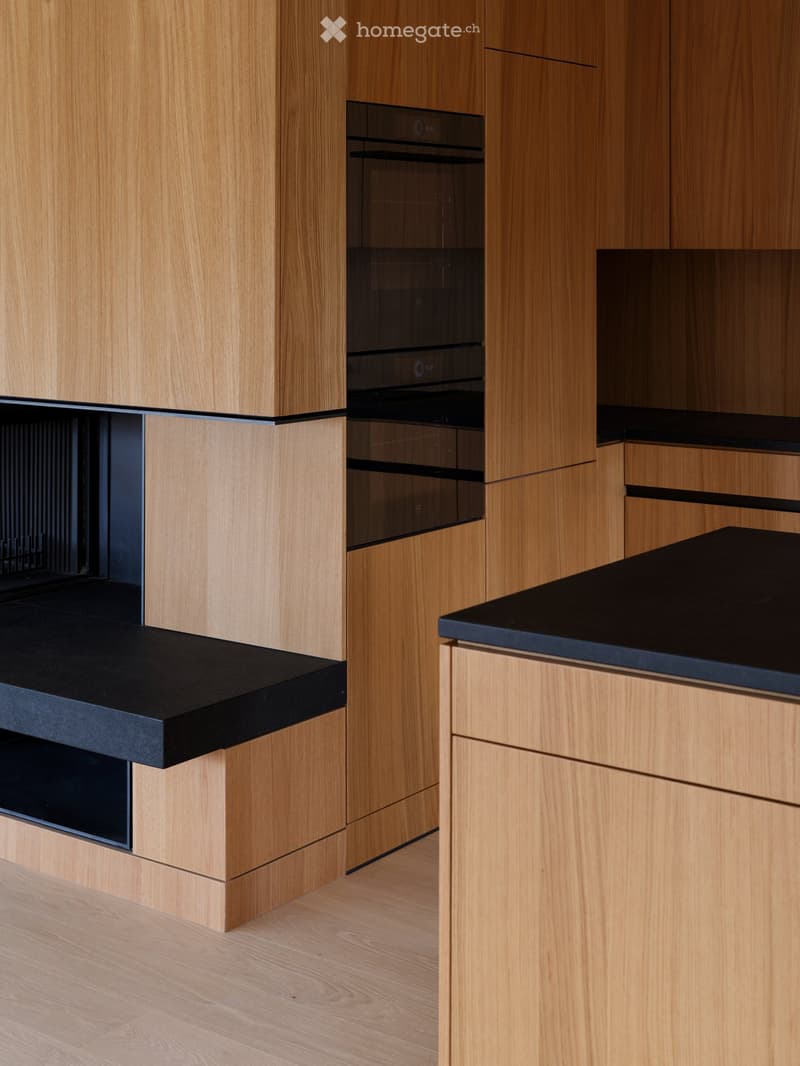 Modern kitchen with light wooden cabinets, black countertop, and built-in oven.