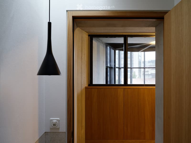 Modern hallway with wooden door frame, pendant light fixture, and large window showing a view of the building exterior.