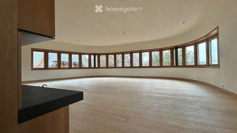 Empty room with wooden flooring, large windows, and a small black countertop on the left side.