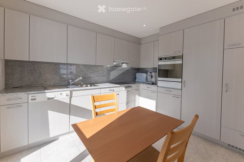modern kitchen with built-in appliances, dishwasher, dining table and chairs, light colored cabinets and tiled flooring