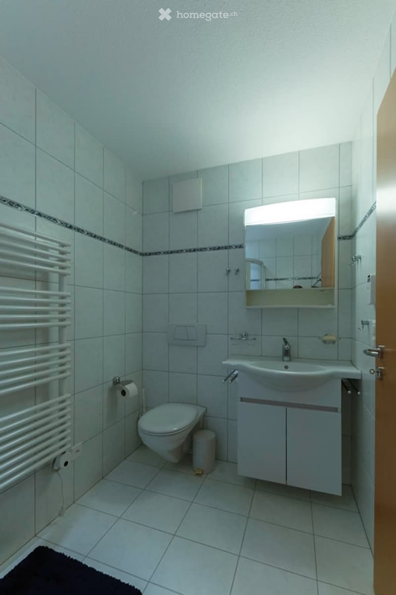 Bathroom with white tiles, toilet, sink, mirror, and towel rack