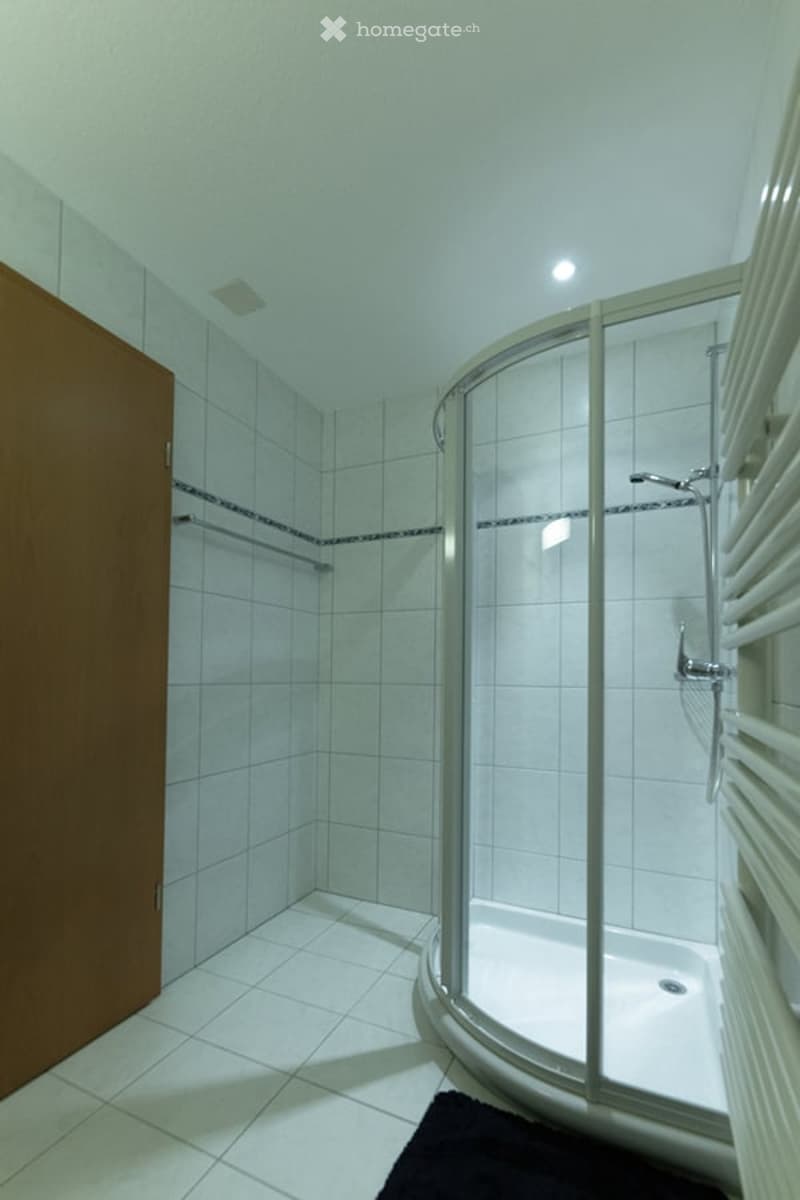 tiled walls, floor, walk-in shower, shower head, faucet, towel rack, wooden door, black mat