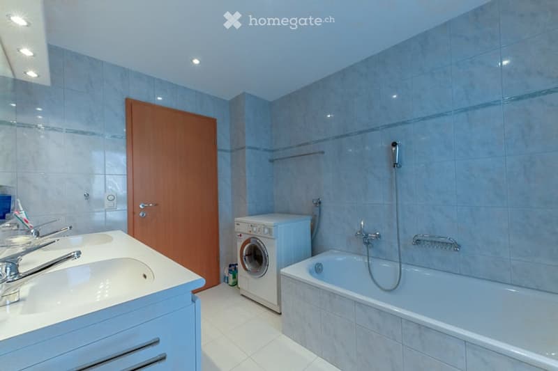 Bathroom with white tiles, blue walls, a sink, bathtub, washing machine, and wooden door