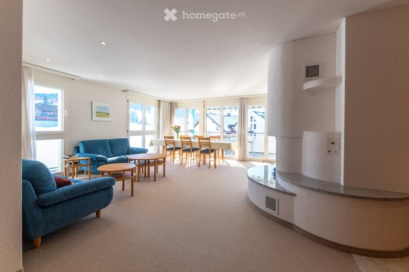 bright space with white walls and white ceiling, two blue couches, round table, rectangular table, dining chairs, flower vase on table, framed picture on wall, open sliding doors
