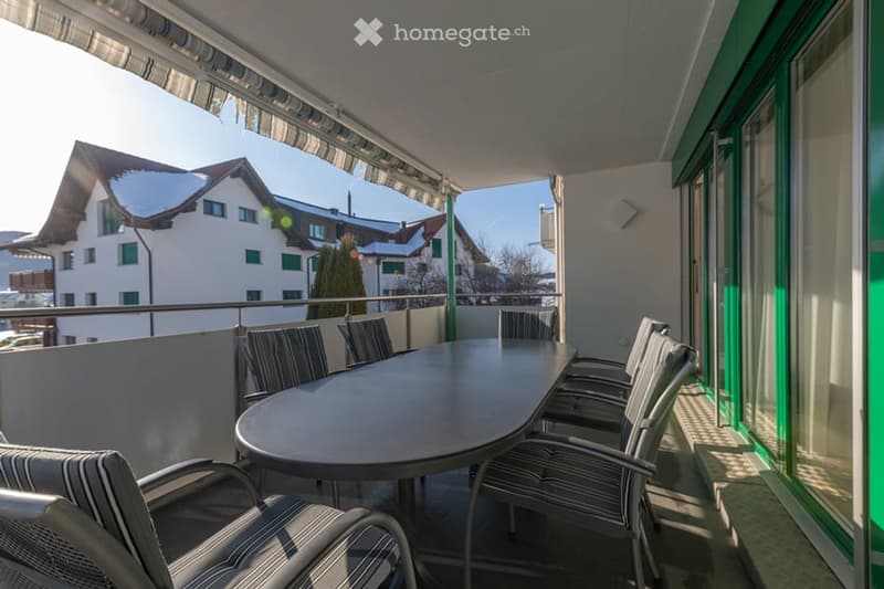 balcony with a dining table and chairs, metal railings, white walls, glass doors, view of the building in the background