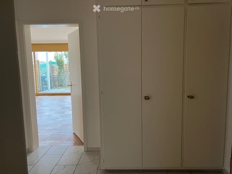 empty room, white tiled floor, white wardrobe, wooden door, sliding glass door, open window with a view of a garden