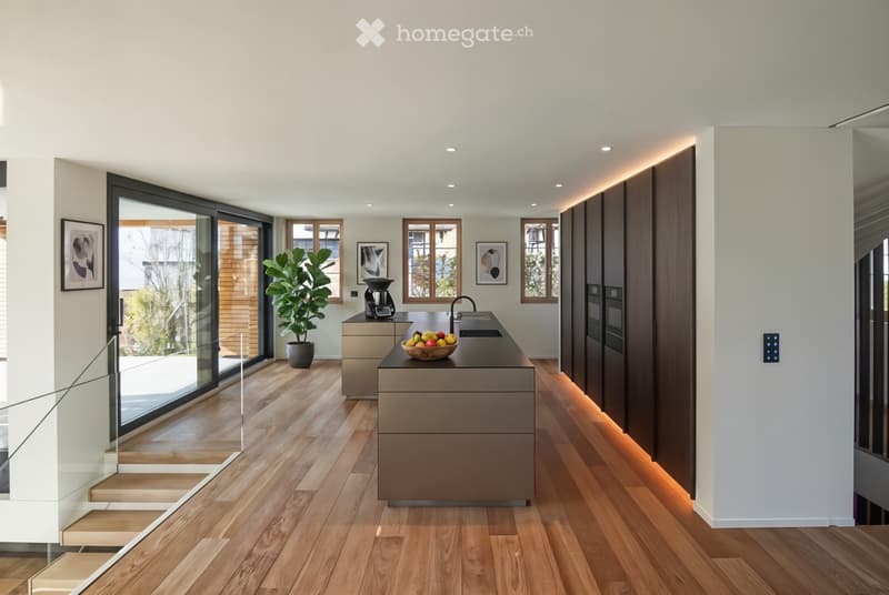 Open kitchen, black countertops, large island, wooden floors, glass windows, wooden staircase, kitchen appliances, potted plant, modern decor, picture frames