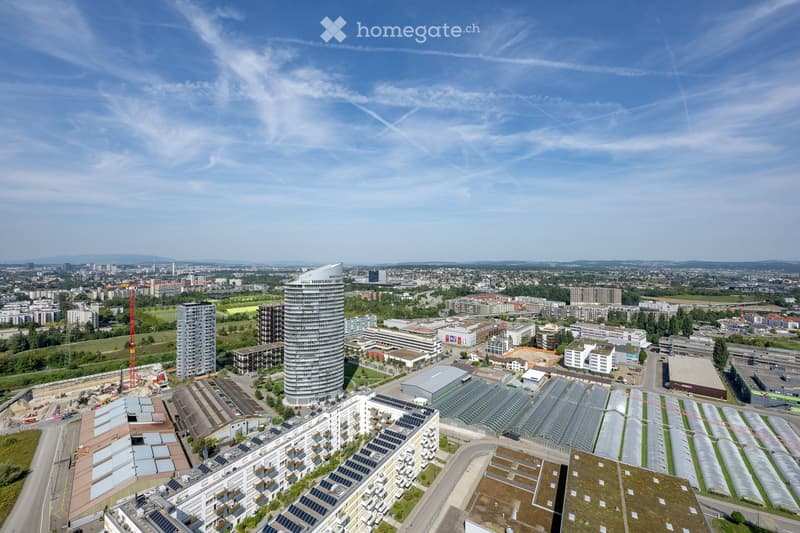 Aerial view of the city, several high-rise buildings and skyscrapers, one being a tall spiral tower, multiple construction sites, solar panels, road, clear blue sky.
