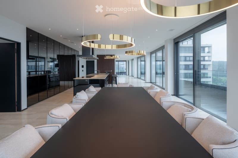 long table, large glass windows, multiple gold circular light fixtures, glass and wood kitchen with countertops and island