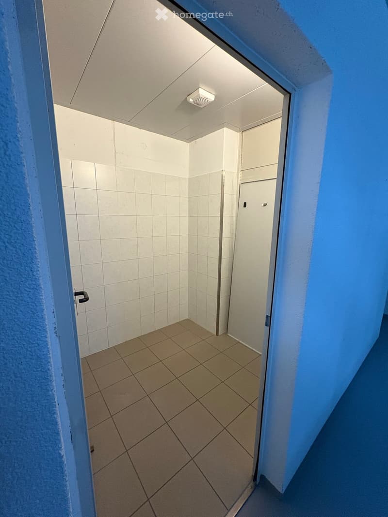 Empty room with tiled floor and walls, white ceiling, open door, and a white door on the right side.