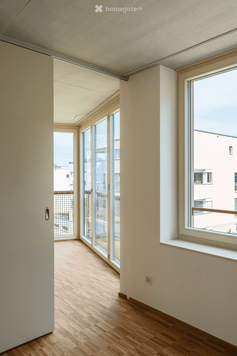 Bright, minimalist hallway with wooden flooring, large windows, and sliding glass doors leading to a balcony area.