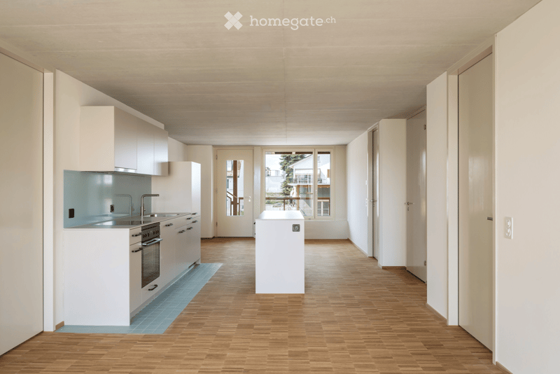 Modern, minimalist kitchen with white cabinets, stainless steel appliances, and wooden flooring. Features a sink, faucet, oven, and refrigerator.