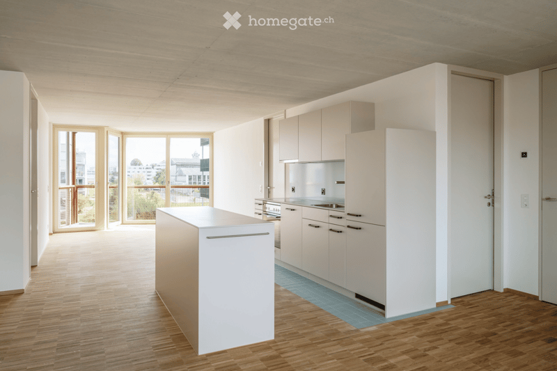Modern kitchen with white cabinets, a central island, and a stove. Large windows and sliding doors lead to a balcony.