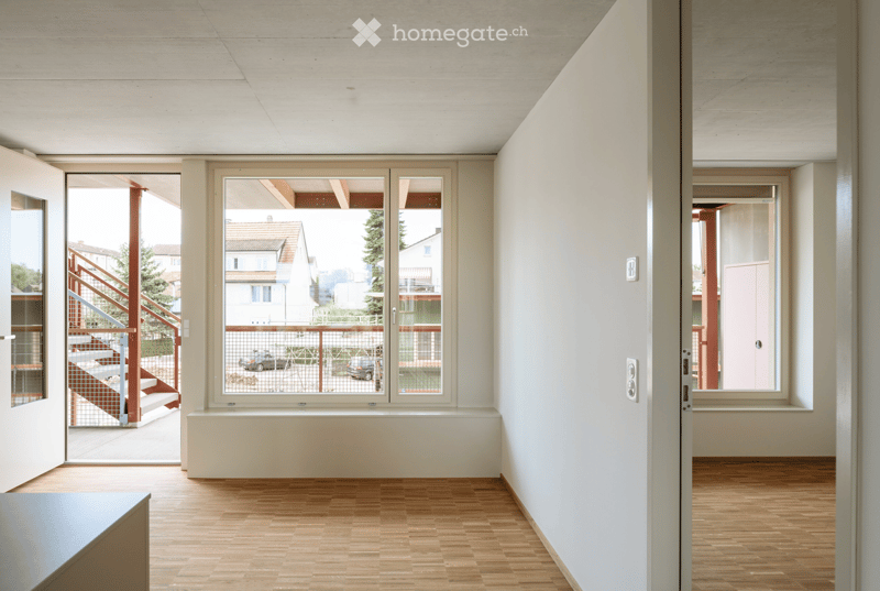 Empty hallway with light wooden flooring, white walls, and large windows offering views of the exterior. No furniture or personal items are present.