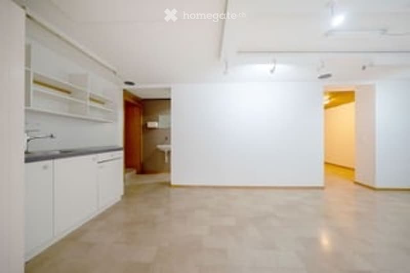 Empty kitchen with white cabinets, tiled floor, sink, and a door leading to another room