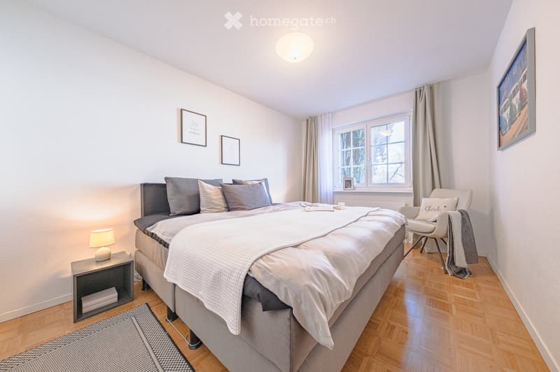 Bedroom with bed, nightstand, chair, rug, lamp, window, curtains, picture frames, radiator