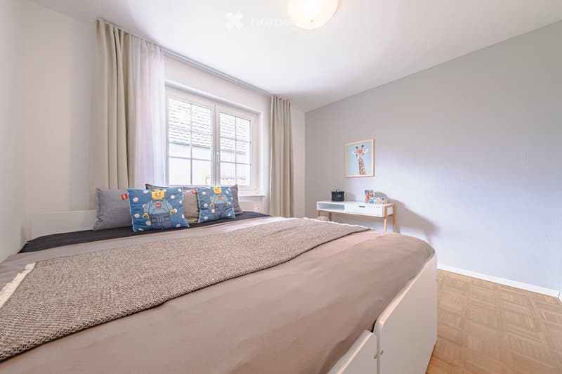 Bedroom with bed, pillows, blanket, desk, picture frame, window with curtains