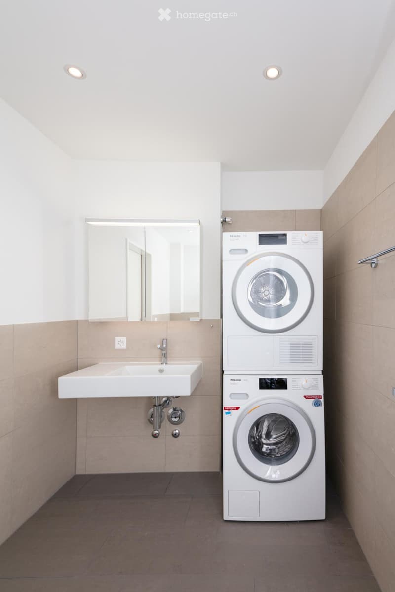 small bathroom with white sink, mirror, and stacked washing machines