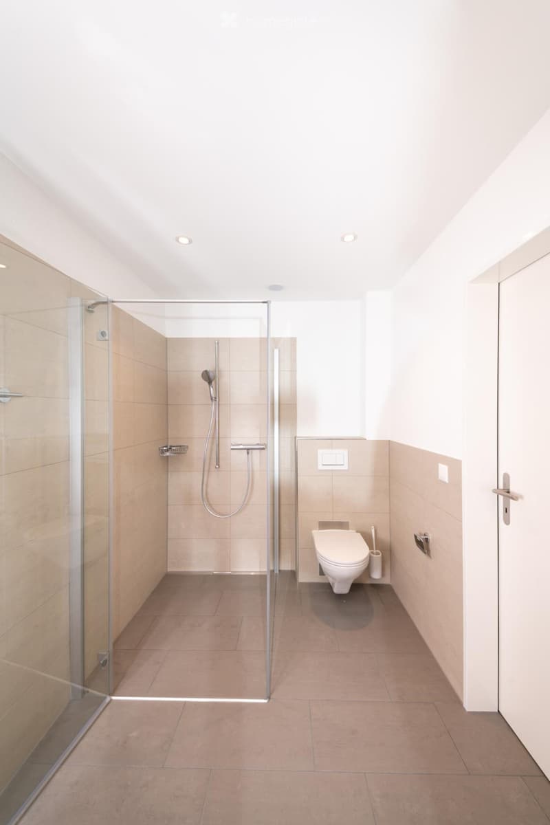 Modern bathroom with glass shower enclosure, beige tiles, white toilet, and white walls.