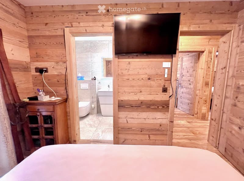 Bedroom with wooden walls, bed, TV, wooden cabinet, bathroom with toilet and sink