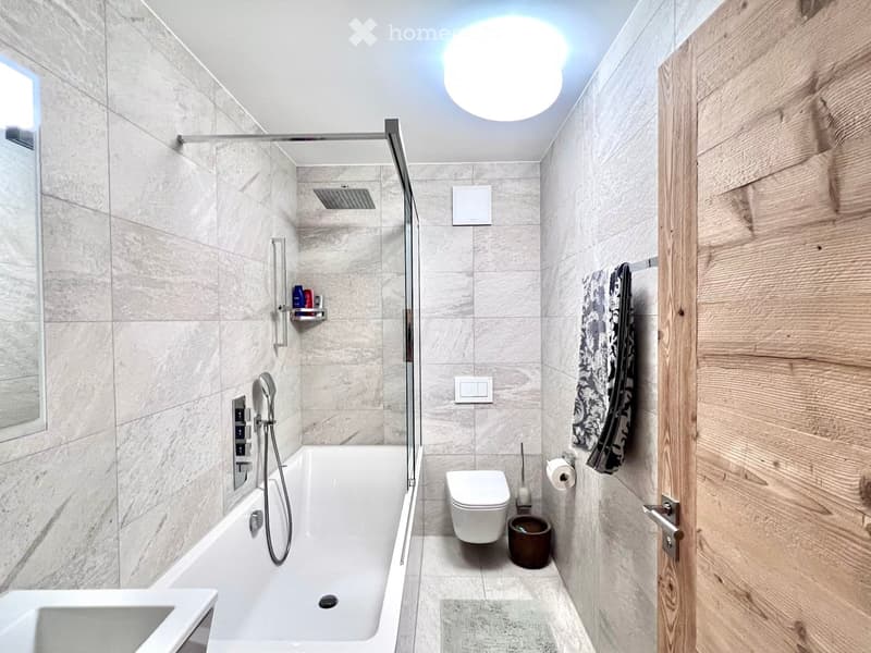 modern bathroom with bathtub, shower, toilet, sink, wooden door, tiled walls, mirror, towel rack, toilet paper