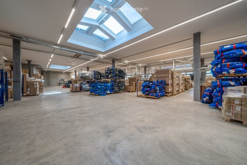 large warehouse, concrete floor, multiple skylights, numerous stacked boxes, blue tarps, metal beams, industrial lighting
