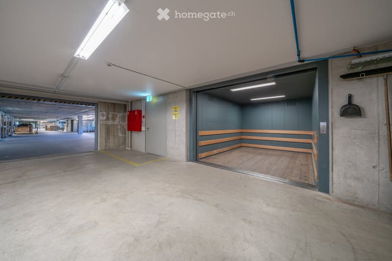 underground parking lot, concrete walls, fluorescent lighting, open elevator, storage room, fire extinguisher