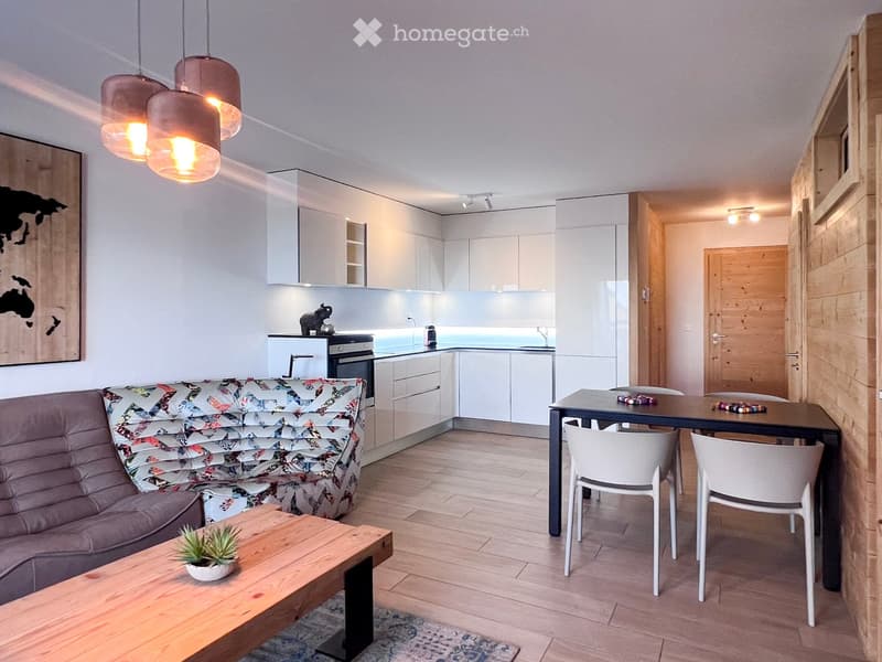 Open plan living room and kitchen, wooden floor, white cabinets, dining table, couch, coffee table, pendant lights, artwork, potted plant