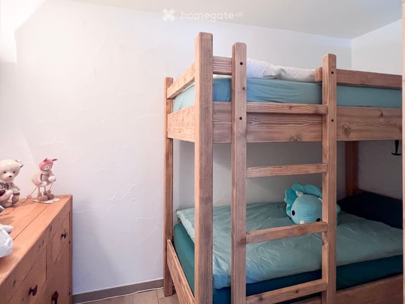A room with a wooden bunk bed, a wooden cabinet, and a white wall.