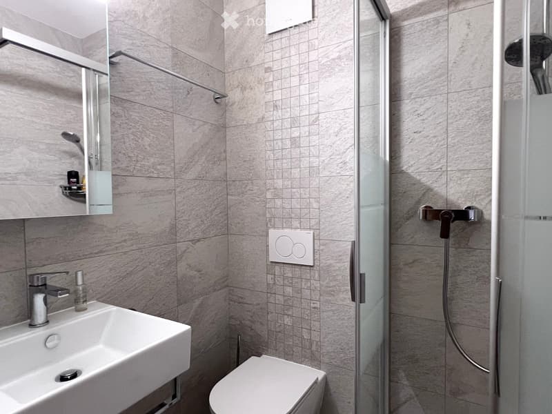 modern bathroom with white sink, white toilet, glass shower enclosure, gray tiles, silver fixtures