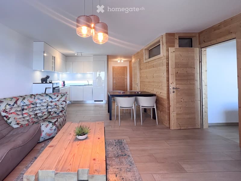 Open living room with dining area, wooden floor, wooden walls, modern furniture, kitchen with appliances, couch, coffee table, rug, and decorative items