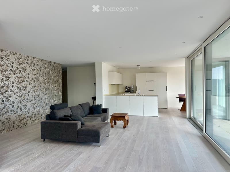 Open floor plan with white walls, hardwood floors, living room with sectional sofa, open kitchen with island and breakfast nook, large sliding glass door to balcony, wall with wallpaper